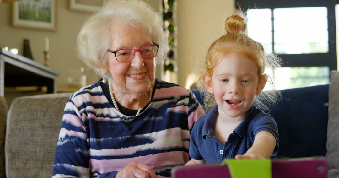 Grandmother with Granddaughter Using Tablet at Home, Both Amused and Smiling - Free Images, Stock Photos and Pictures on Pikwizard.com