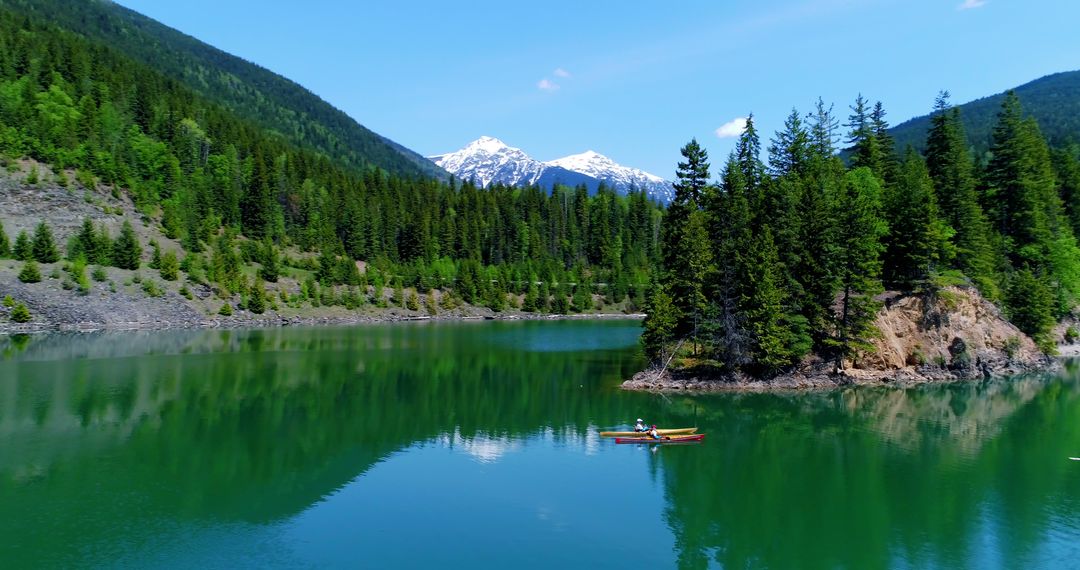 A person kayaks on a serene lake against a backdrop of a forest and snow-capped mountain. - Free Images, Stock Photos and Pictures on Pikwizard.com