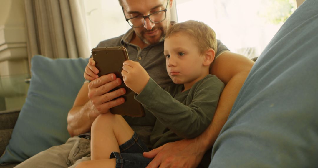 Father and Son Using Digital Tablet Relaxing on Couch - Free Images, Stock Photos and Pictures on Pikwizard.com