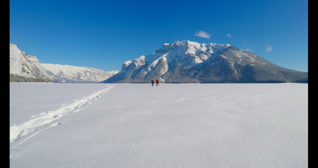 Two hikers walking on snow-covered mountain landscape under clear blue sky - Free Images, Stock Photos and Pictures on Pikwizard.com