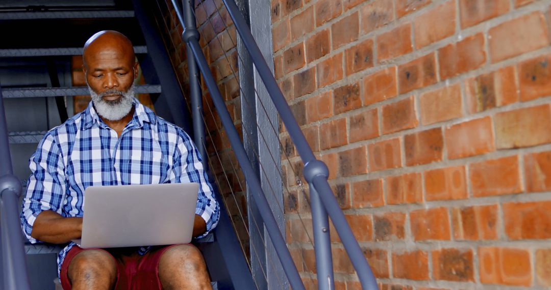 Elderly African-American Man Using Laptop on Staircase - Free Images, Stock Photos and Pictures on Pikwizard.com