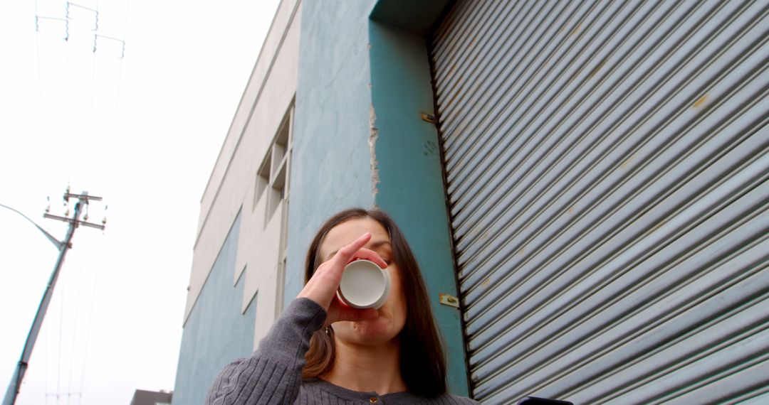 Woman Drinking Coffee Outdoors Near Shuttered Building - Free Images, Stock Photos and Pictures on Pikwizard.com