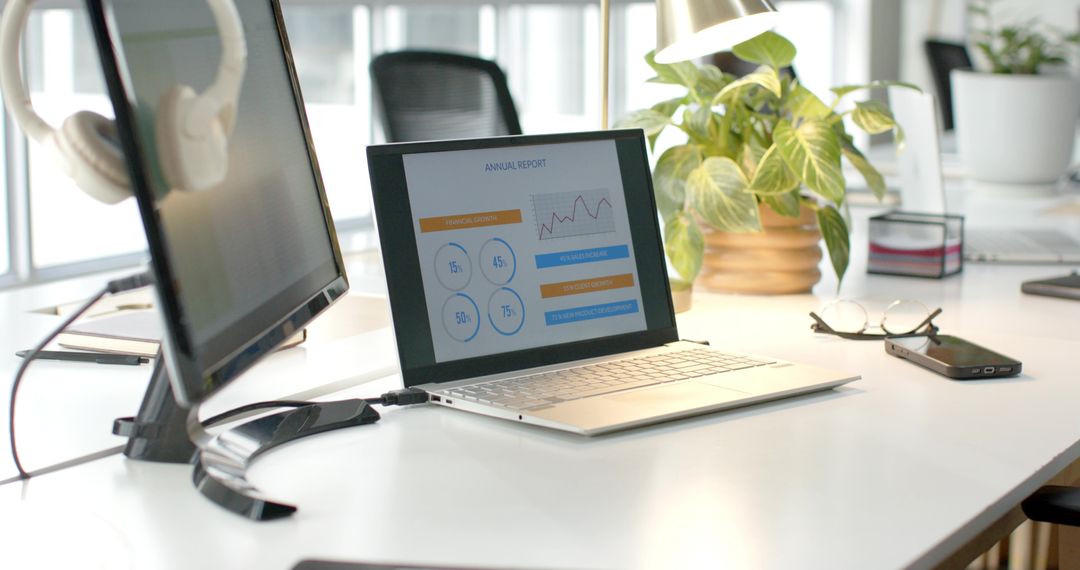 Laptop displaying annual report on bright modern desk with monitor and plant