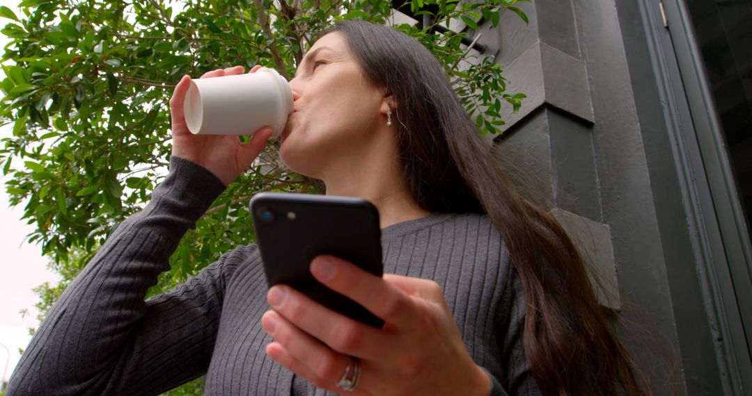 Low Angle View of Happy Woman Using Mobile Phone in City with Coffee - Free Images, Stock Photos and Pictures on Pikwizard.com