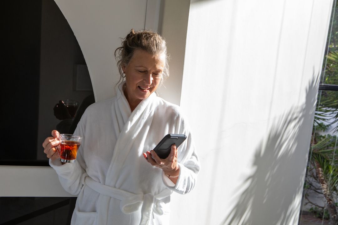 Senior Woman Relaxing with Smartphone and Tea in Bright Environment