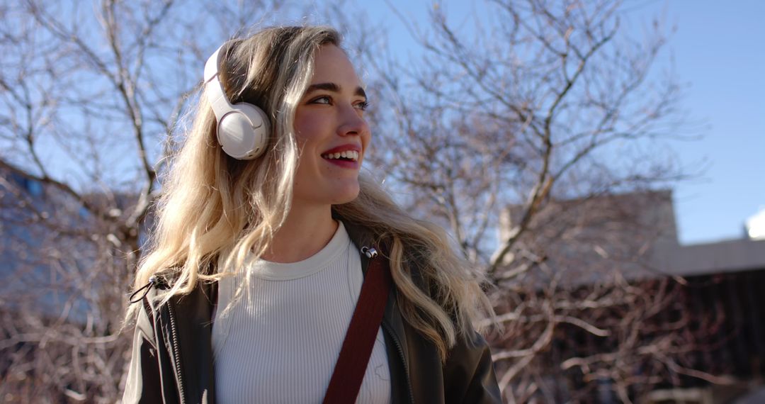 Young woman listening to music with headphones while walking through urban sunlight