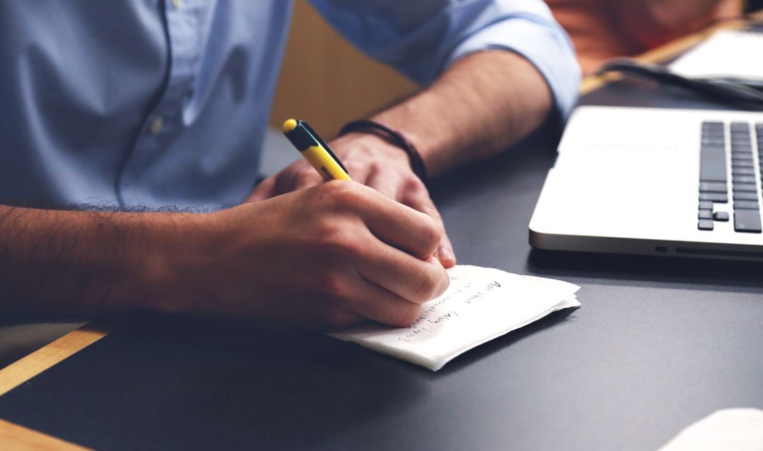 Person Taking Notes Beside Laptop in Study Environment