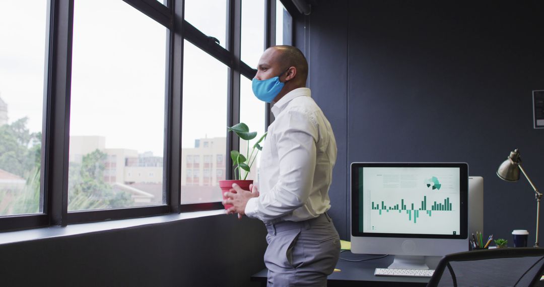 Young Black Businessman Holding Plant in Office, Wearing Face Mask, Standing by the Window - Free Images, Stock Photos and Pictures on Pikwizard.com