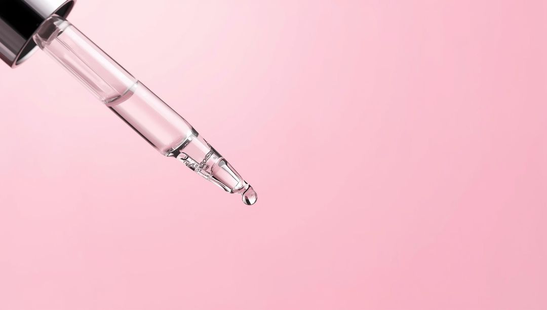 Glass Dropper Pipette with Clear Liquid on Pink Background
