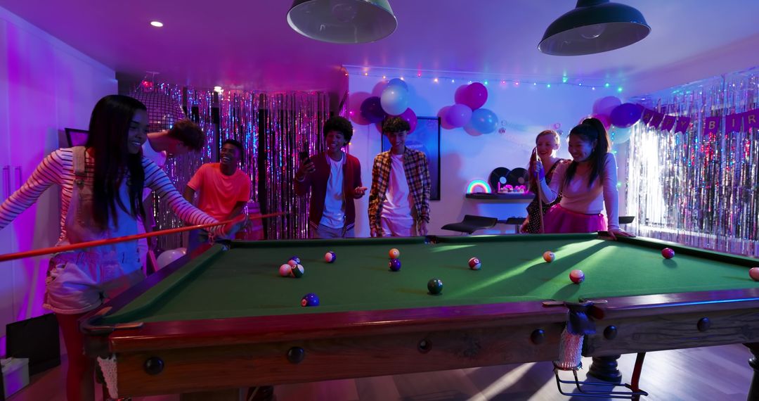 Diverse Friends Playing Pool at Neon Party with Balloons, Tinsel and Festive Lighting