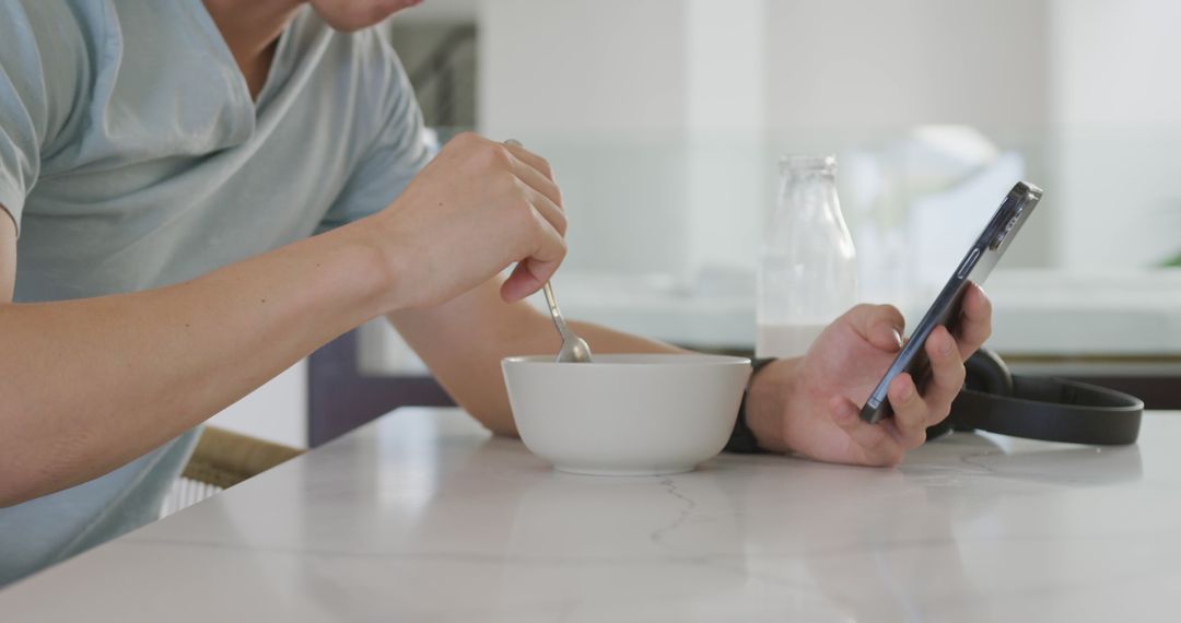 Person Eating Breakfast While Using Smartphone at Kitchen Counter - Free Images, Stock Photos and Pictures on Pikwizard.com