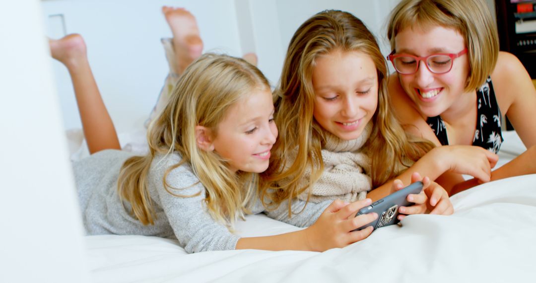 Three Girls Lying on Bed and Smiling While Playing with Smartphone - Free Images, Stock Photos and Pictures on Pikwizard.com