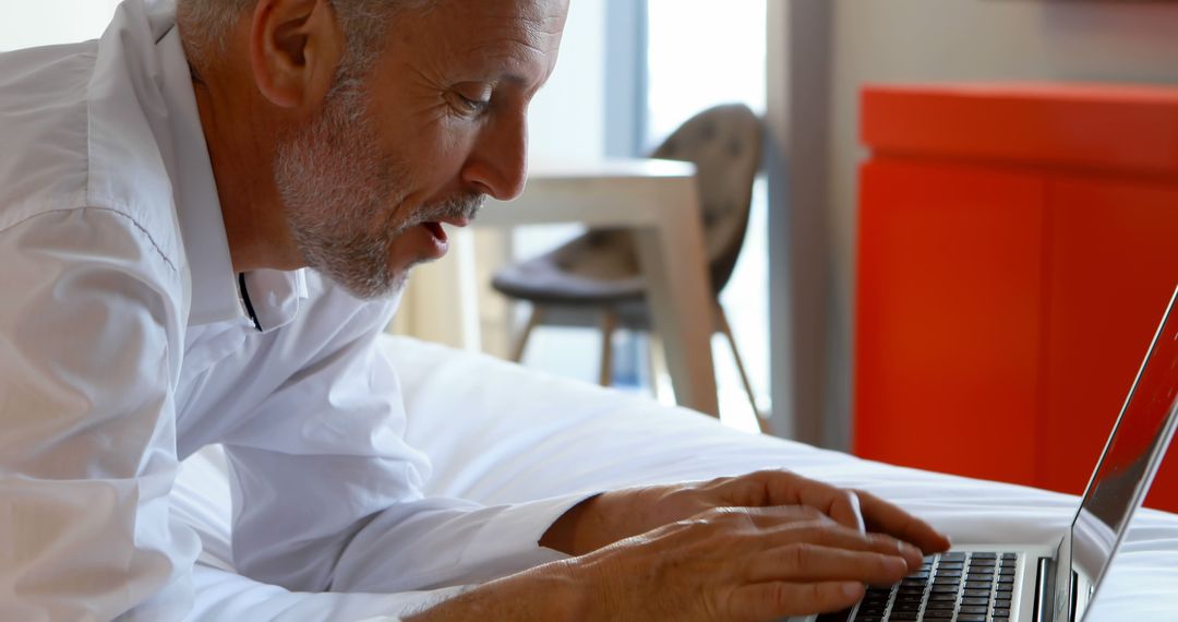 Middle Aged Man Working on Laptop While Lying on Bed in Modern Home - Free Images, Stock Photos and Pictures on Pikwizard.com