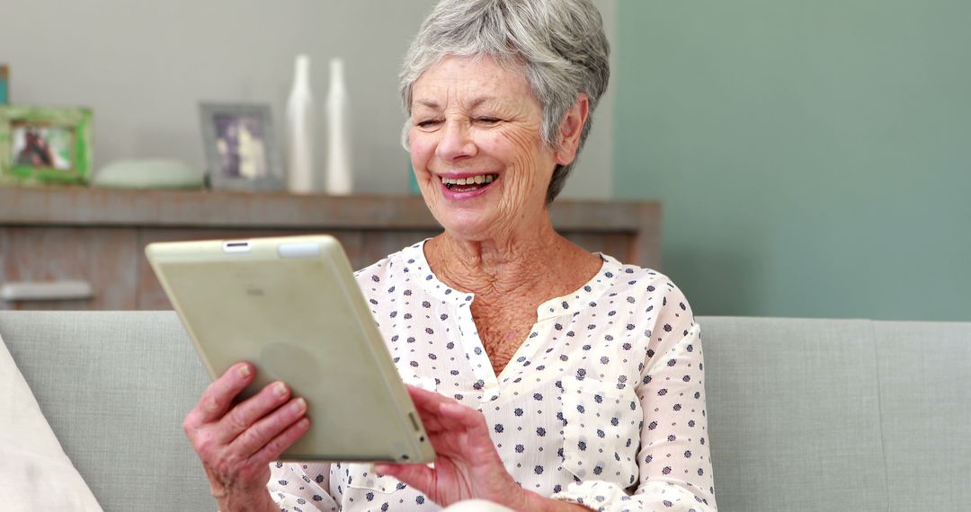 Joyful Elderly Woman Using Tablet on Sofa at Home - Free Images, Stock Photos and Pictures on Pikwizard.com