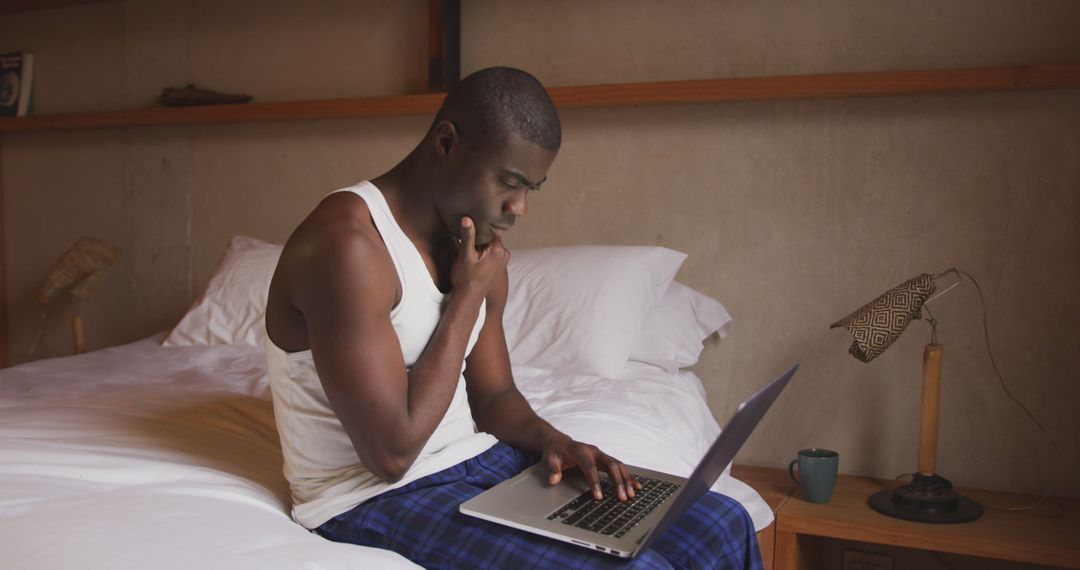 Focused Man Using Laptop Deep in Thought Sitting on Bed at Home