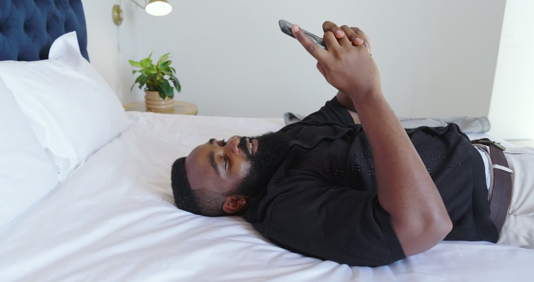Man Relaxing on Bed Using Smartphone in Modern Minimalist Bedroom