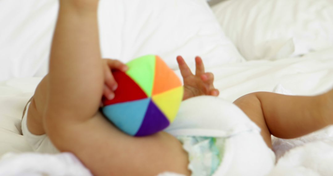 Baby Lying in Bed Holding Colorful Toy Ball - Free Images, Stock Photos and Pictures on Pikwizard.com