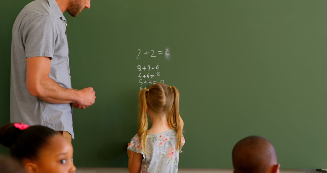 Teacher Assisting Schoolgirl with Math Problem on Chalkboard