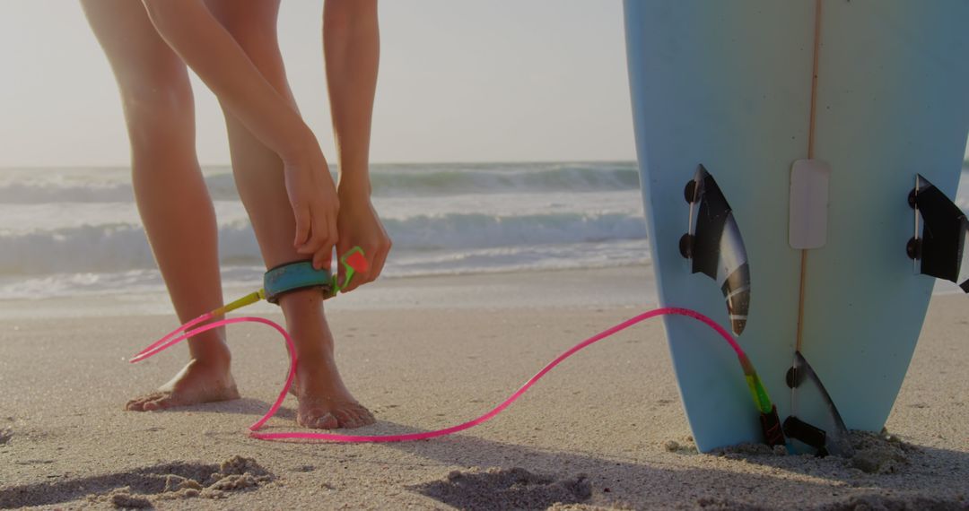 Surfer Tying Leash to Surfboard on Sandy Beach