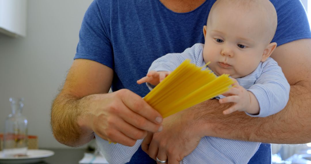 Father Holding Baby Reaching for Dry Spaghetti in Kitchen - Free Images, Stock Photos and Pictures on Pikwizard.com