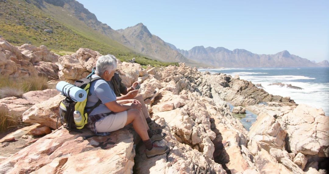 Senior Hikers Resting on Rocky Coast with Ocean and Mountain Views - Free Images, Stock Photos and Pictures on Pikwizard.com