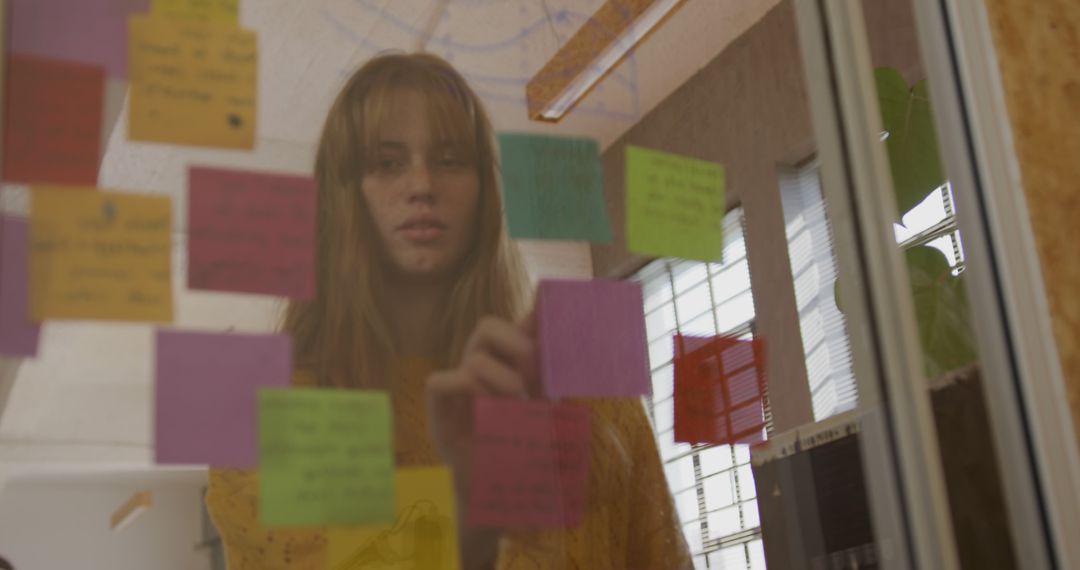 Young Woman Organizing Sticky Notes on Glass Wall in Office - Free Images, Stock Photos and Pictures on Pikwizard.com