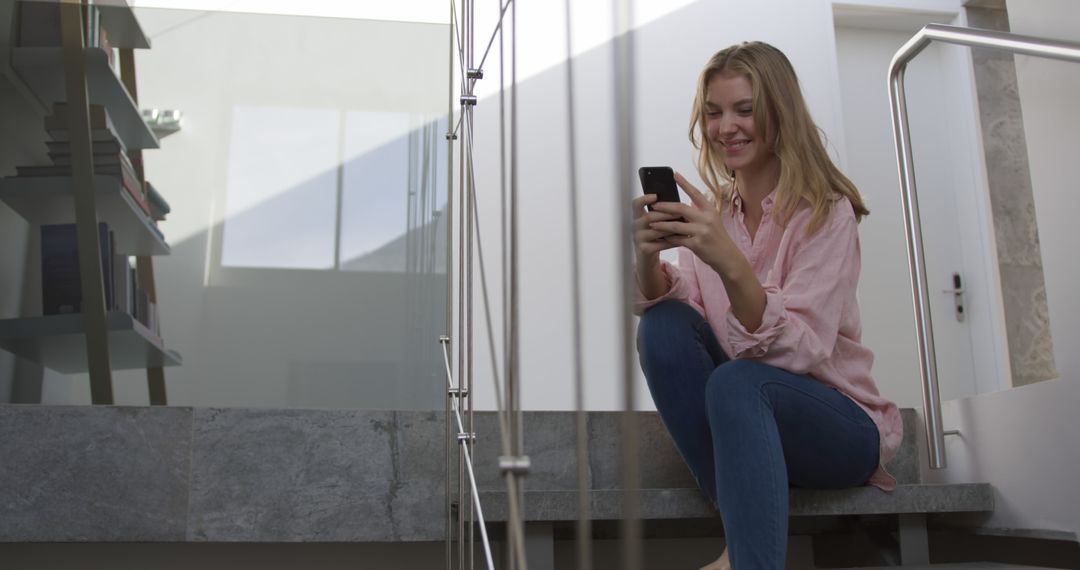 Young woman using smartphone on stairs in modern home - Free Images, Stock Photos and Pictures on Pikwizard.com