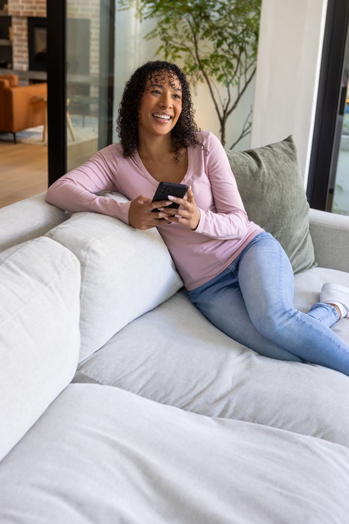 Smiling Woman Relaxing with Smartphone on Comfortable Modern Sofa