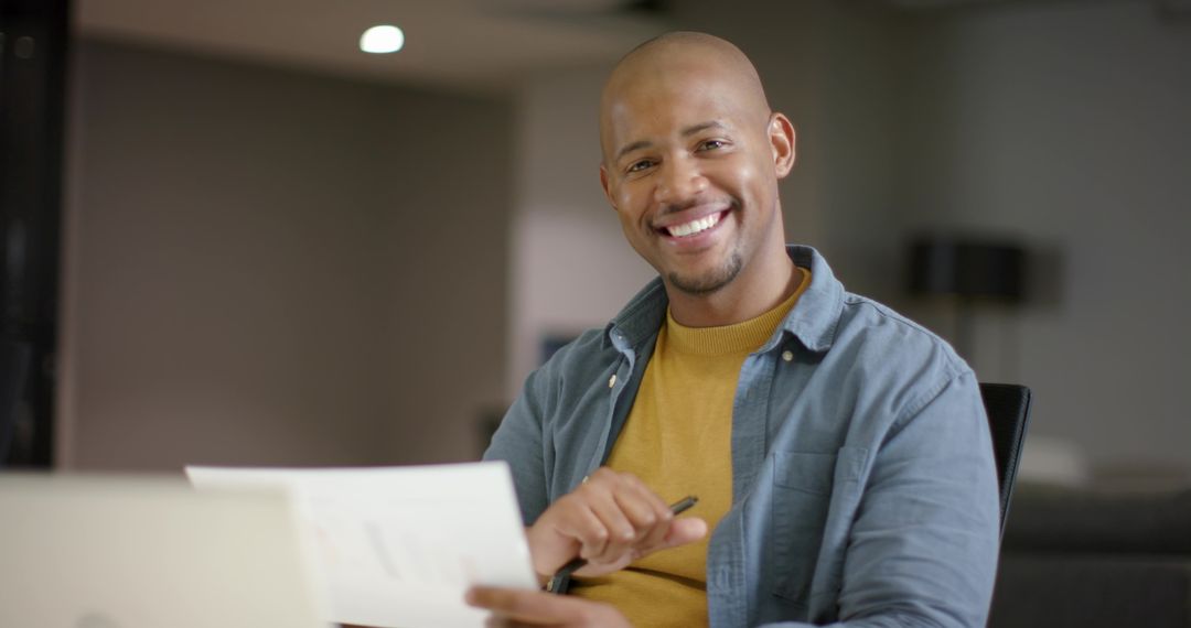 African American man smiling while reviewing documents at modern office desk with laptop