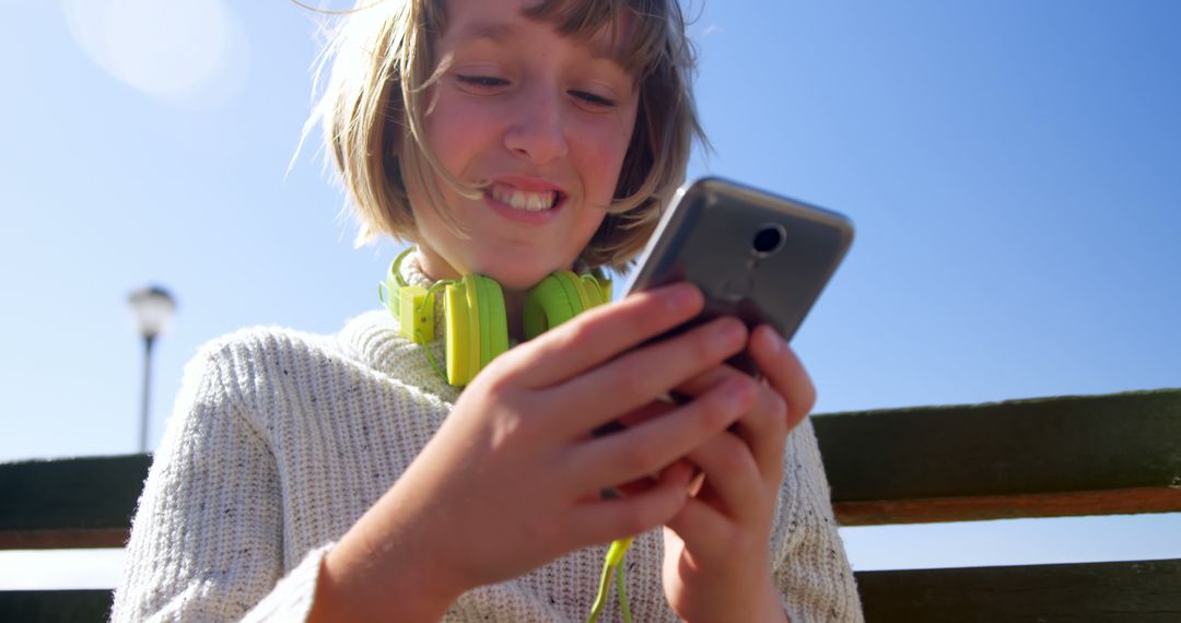 Happy Girl Enjoying Smartphone with Green Headphones Outdoors - Free Images, Stock Photos and Pictures on Pikwizard.com