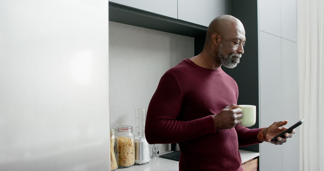 Mature Man Holding Coffee Mug Checking Smartphone in Modern Kitchen - Free Images, Stock Photos and Pictures on Pikwizard.com