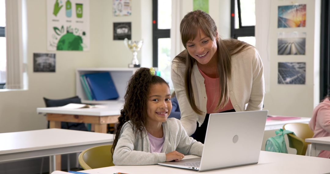 Female Teacher Assisting Smiling Student Using Laptop in Classroom