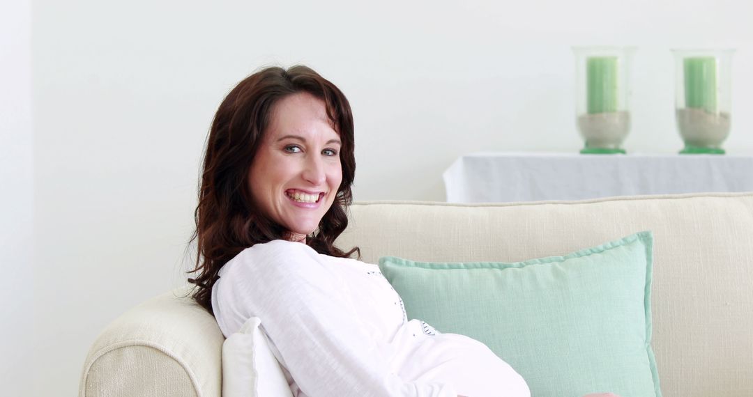 Pregnant woman smiling while sitting on sofa in bright living room - Free Images, Stock Photos and Pictures on Pikwizard.com