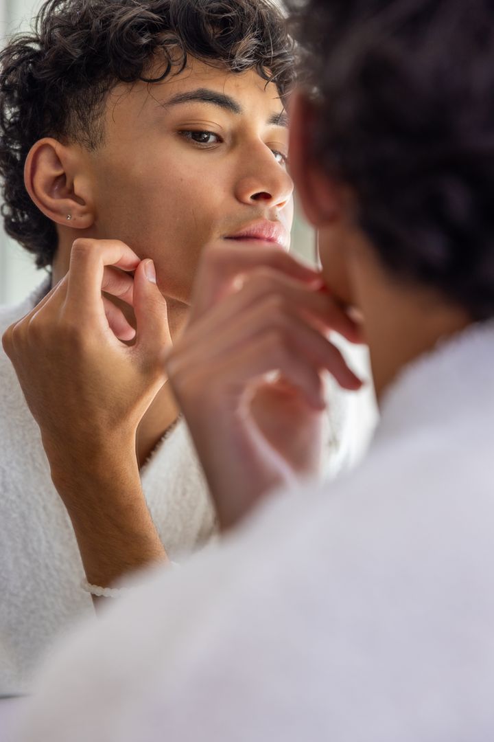 Young Man Adjusting Stud Earring in Mirror Reflection