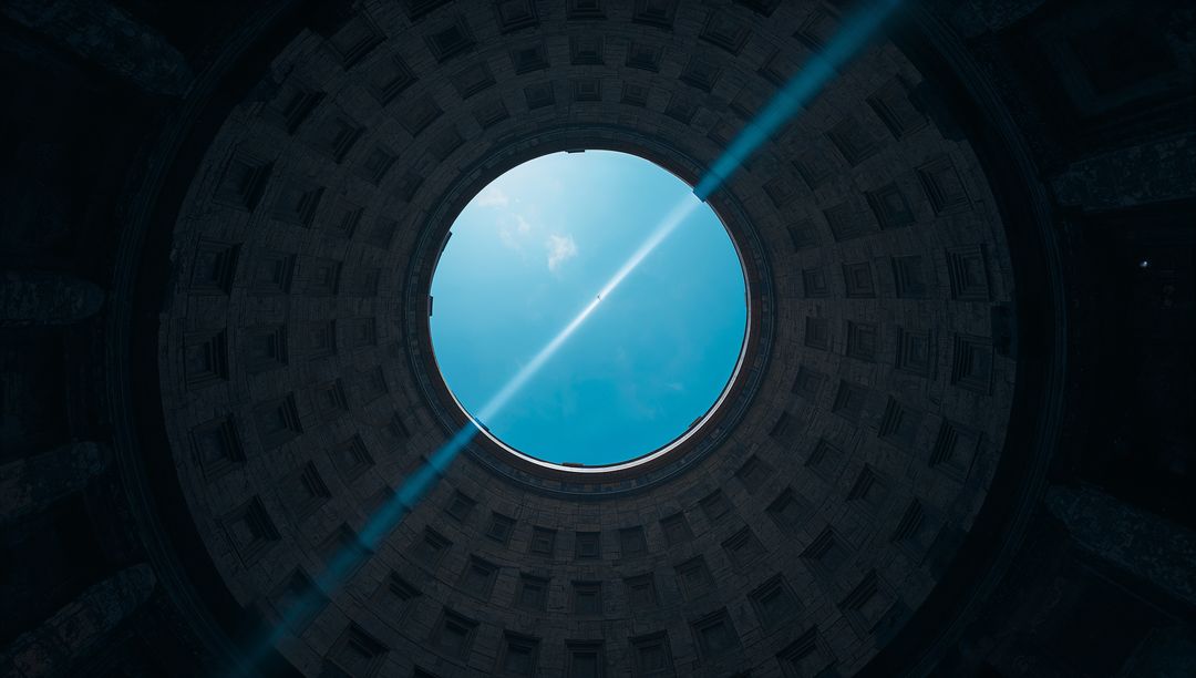 Circular oculus framing bright blue sky with sunbeam through classical dome geometry