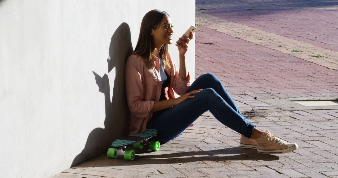 Young Woman Sitting with Skateboard Using Smartphone Outdoors - Free Images, Stock Photos and Pictures on Pikwizard.com