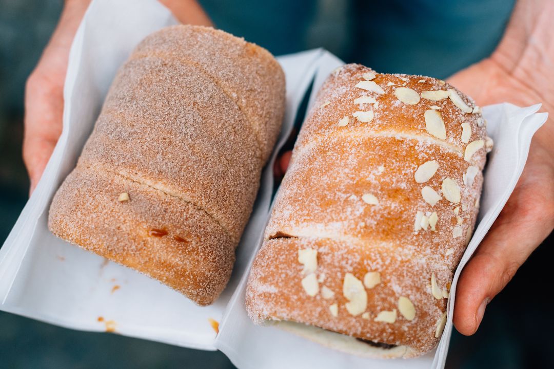 Hands Holding Traditional Chimney Cakes Coated in Sugar and Almonds