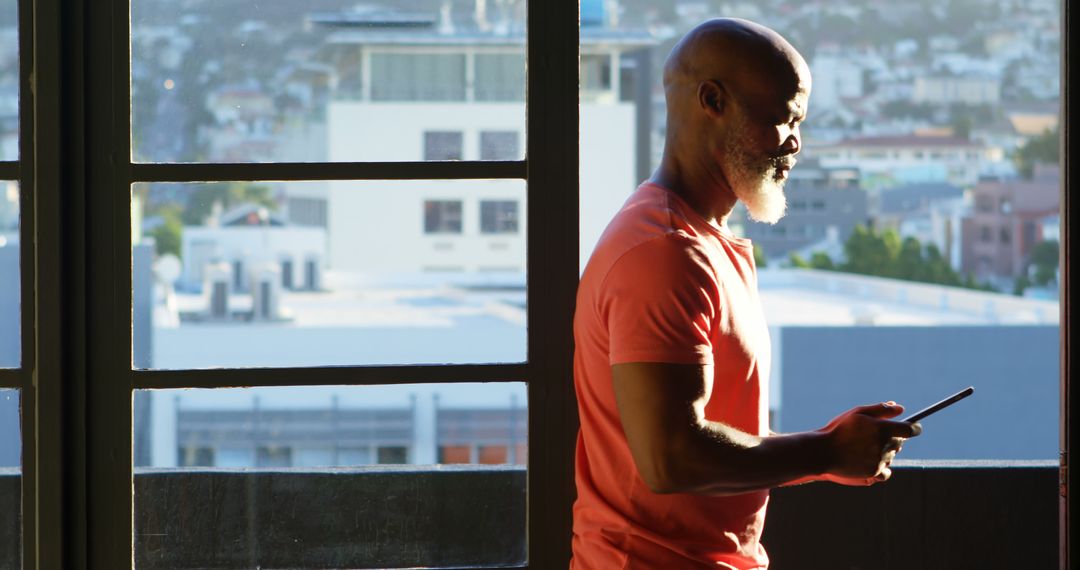 Man with Smartphone Standing by Window Overlooking Urban Area - Free Images, Stock Photos and Pictures on Pikwizard.com