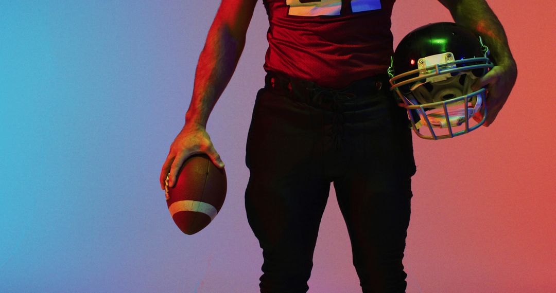 A football player holds a ball against a vibrant neon backdrop, symbolizing athletic rivalry. - Free Images, Stock Photos and Pictures on Pikwizard.com