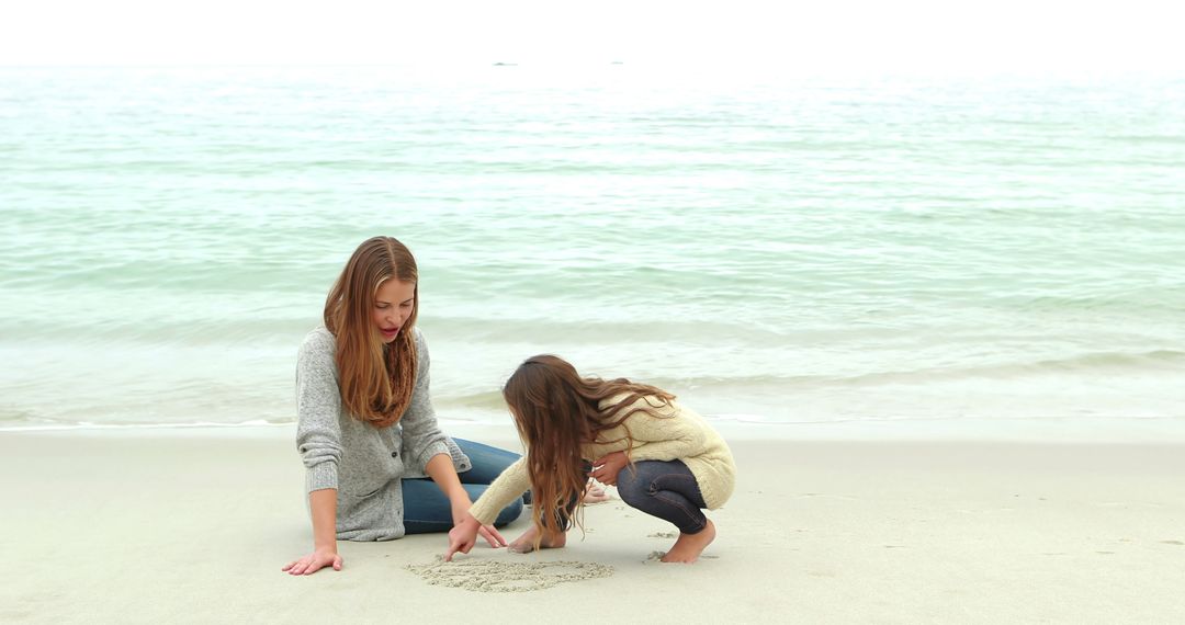 Mother and Daughter Drawing in Sand by Ocean Shore - Free Images, Stock Photos and Pictures on Pikwizard.com