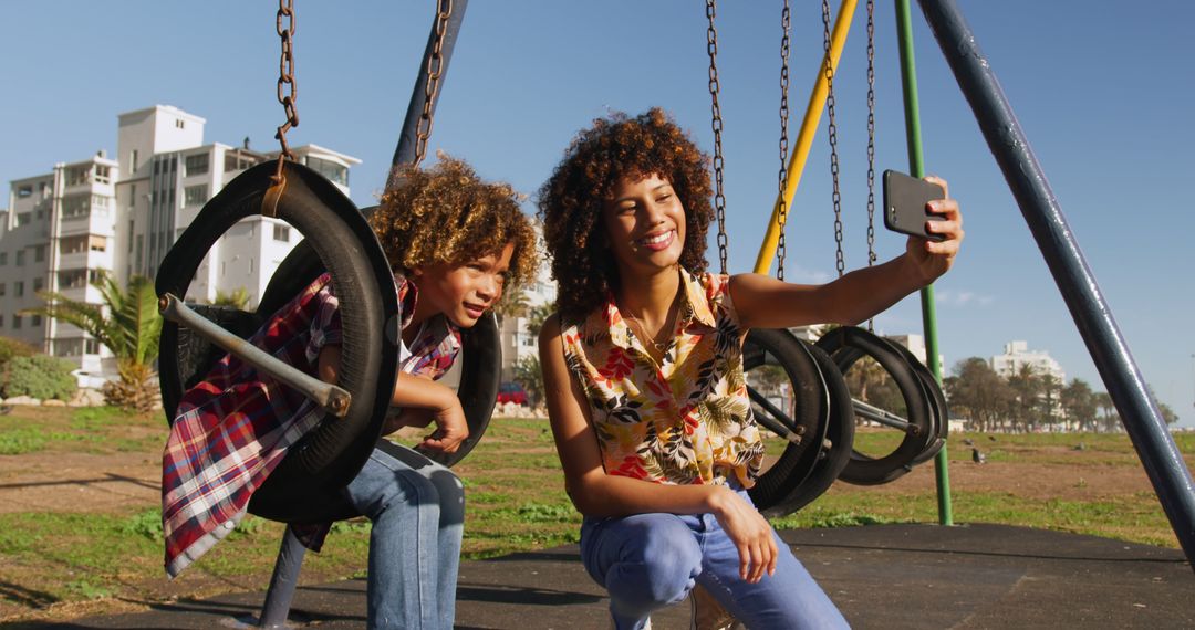 Happy biracial mother taking selfie with son on swing at sunny playground - Free Images, Stock Photos and Pictures on Pikwizard.com