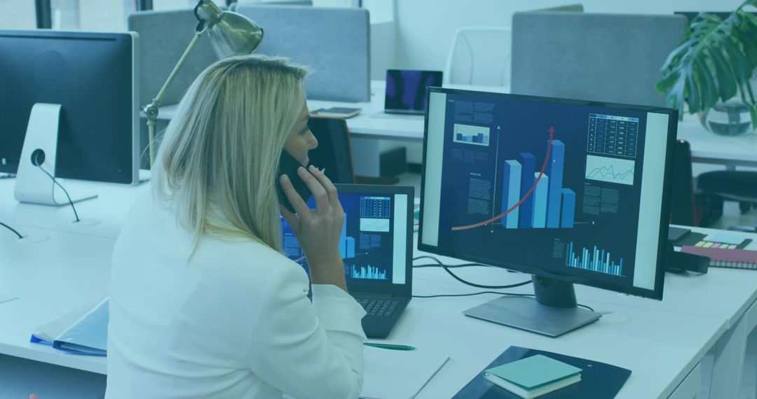 Businesswoman Analyzing Data on Computer and Phone in Modern Office