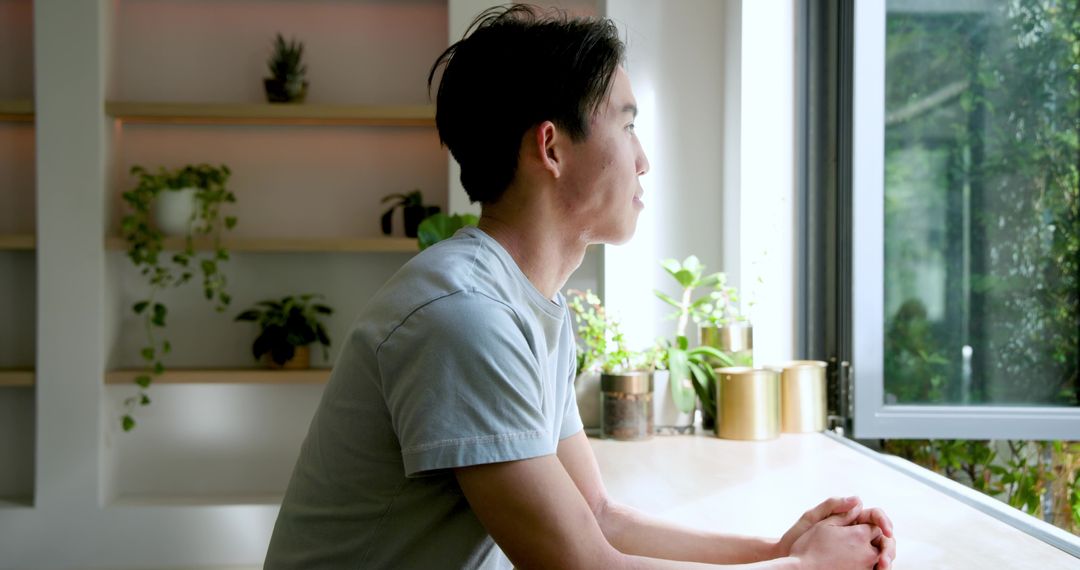 Contemplative Asian Man by Window with Indoor Greenery
