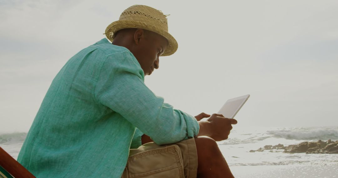 Man Relaxing on Beach Reading Digital Tablet with Ocean Backdrop