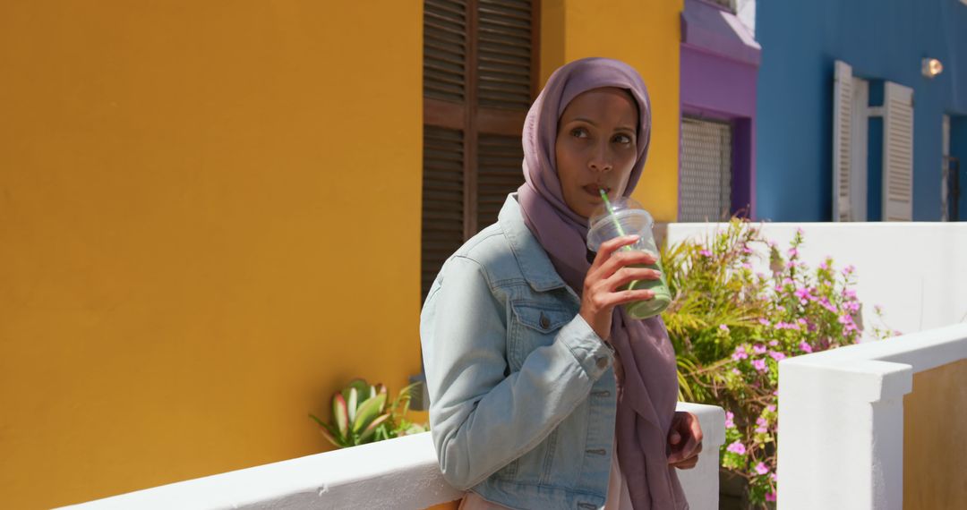 Muslim woman drinking juice standing on colorful urban street - Free Images, Stock Photos and Pictures on Pikwizard.com