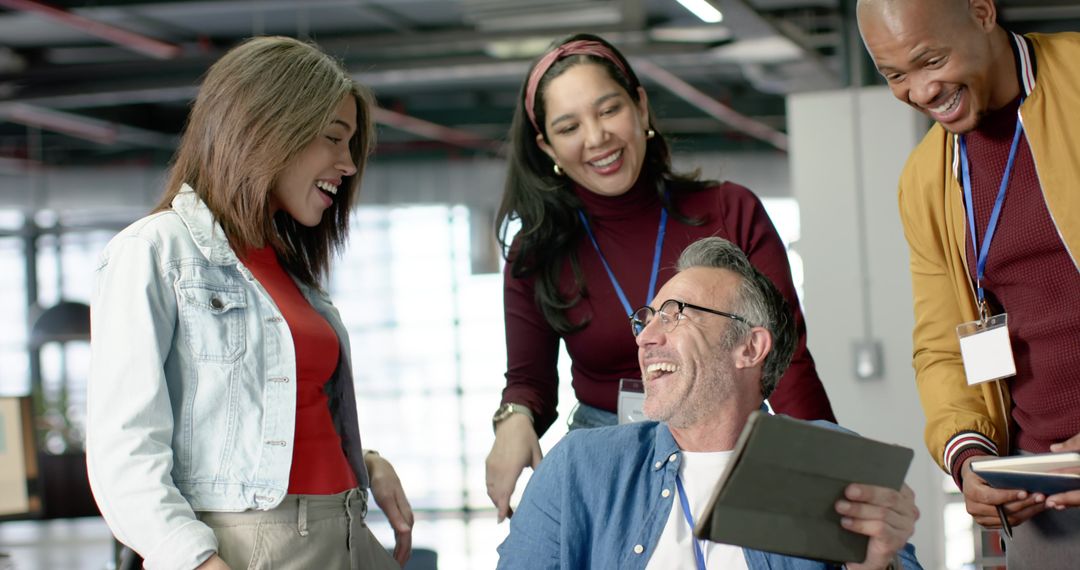 Diverse team collaborating and laughing around tablet in modern office workspace