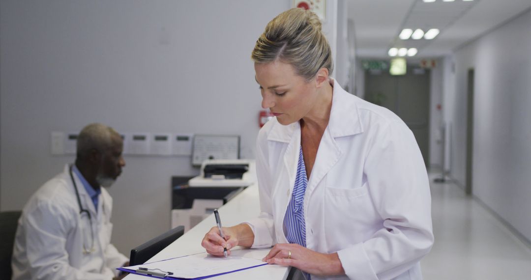 Healthcare Professionals Writing on Clipboard in Hospital Corridor - Free Images, Stock Photos and Pictures on Pikwizard.com