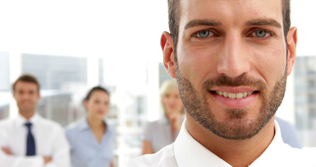 Confident businessman smiling with colleagues in background in office - Free Images, Stock Photos and Pictures on Pikwizard.com