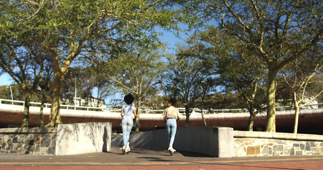 Two Women Walking in Urban Park on Sunny Day - Free Images, Stock Photos and Pictures on Pikwizard.com