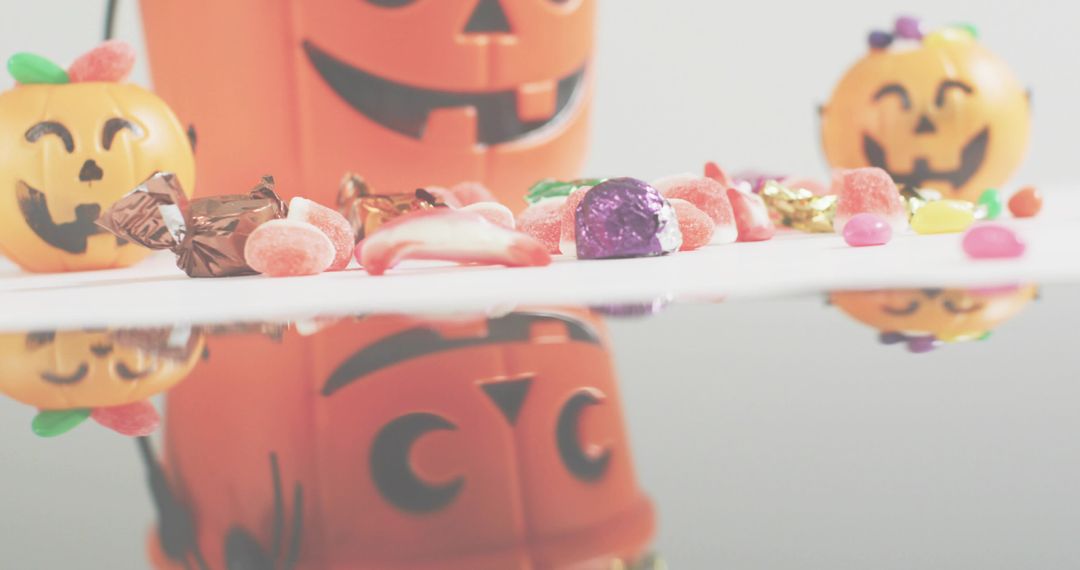Reflecting Halloween candies and jack-o-lantern buckets on glossy studio tabletop